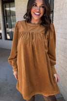 Woman wearing DESERT WINDS Dress in copper corduroy with puff sleeves and pleats, showcasing elegance and femininity.