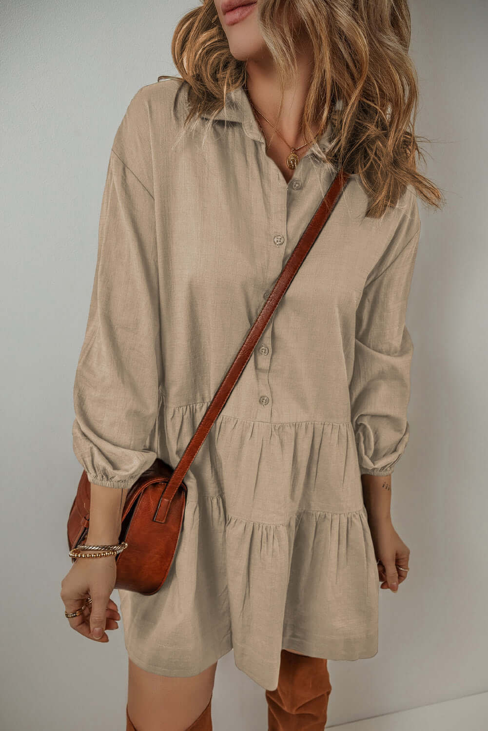 Woman wearing VENTURE OUT Desert Tan mini dress with puff sleeves, buttoned front, and tiered design, paired with a brown crossbody bag.