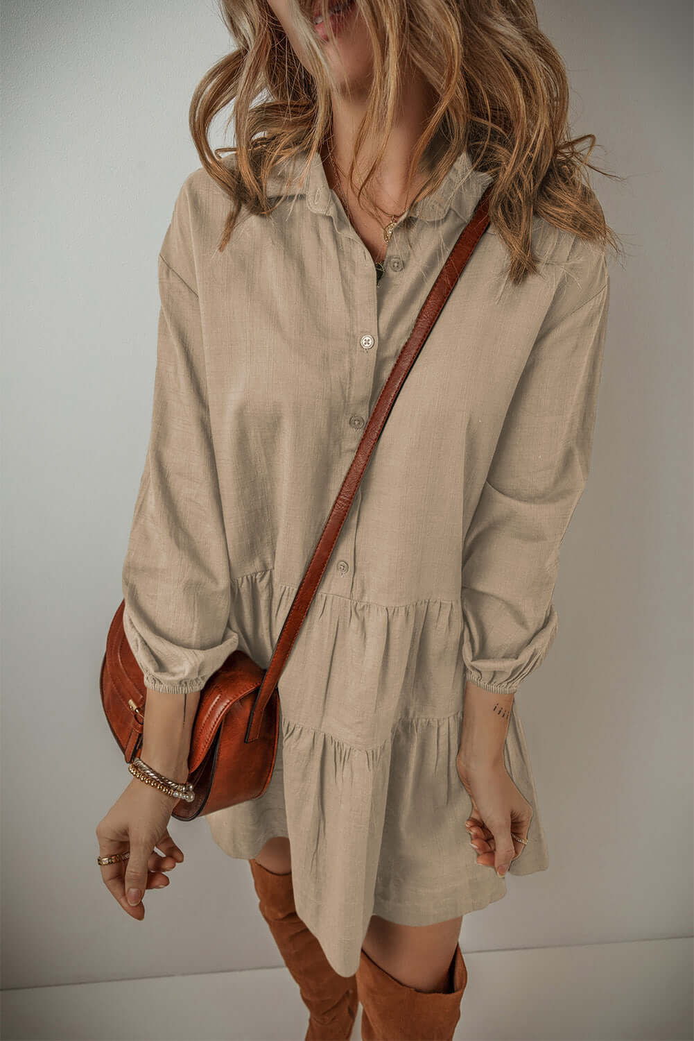 Woman wearing VENTURE OUT Desert Tan mini dress with puff sleeves and buttoned front, paired with a brown leather crossbody bag.