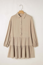 Desert Tan mini dress with puff sleeves, buttoned front, and tiered pleats hanging on a wooden hanger, showcasing chic style.