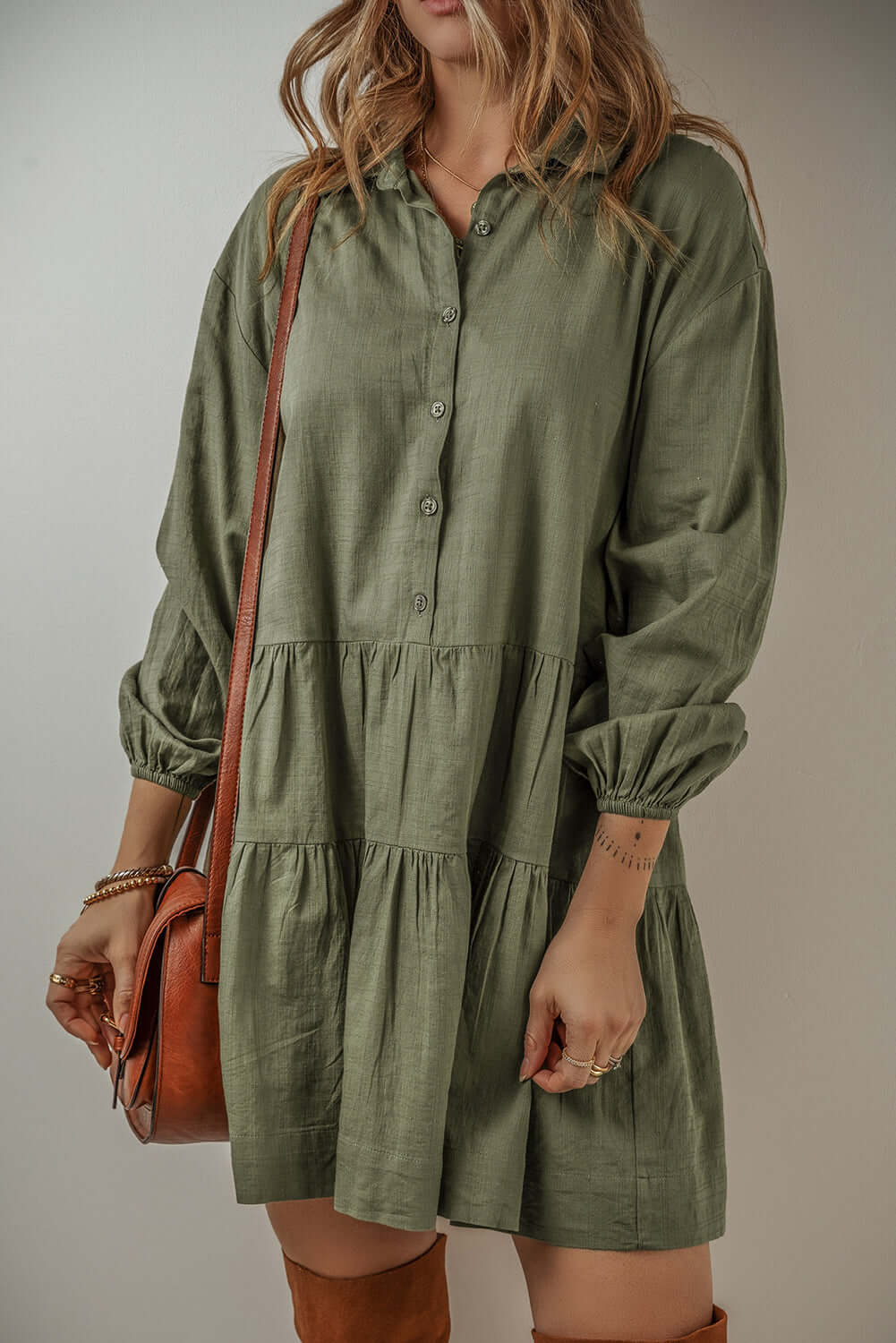 Woman wearing a Jungle Green VENTURE OUT mini dress with puff sleeves, buttoned front, and tiered design, accessorized with a brown bag.