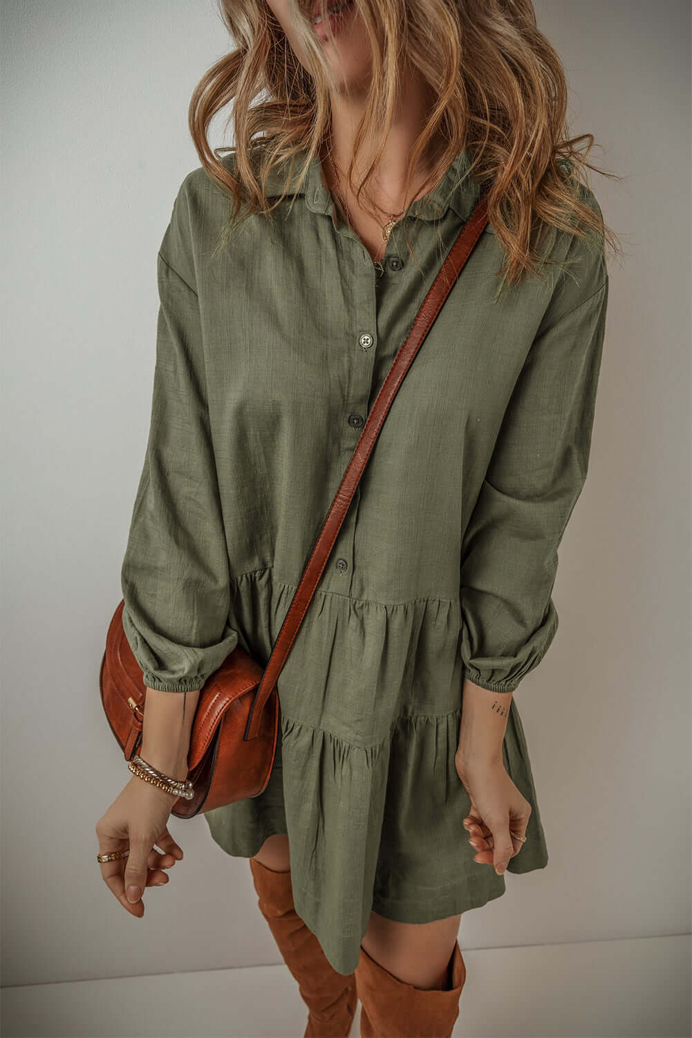 Woman wearing a jungle green mini dress with puff sleeves and buttoned front, styled with a brown leather bag and boots.