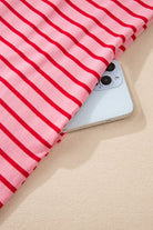 Close-up of a striped fabric with pink and red colors, showcasing the STRAWBERRY SUNDAYS DRESS alongside a smartphone.