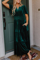 Woman wearing Elegant Emerald Maxi dress with short sleeves and V-neck, standing by a green door.