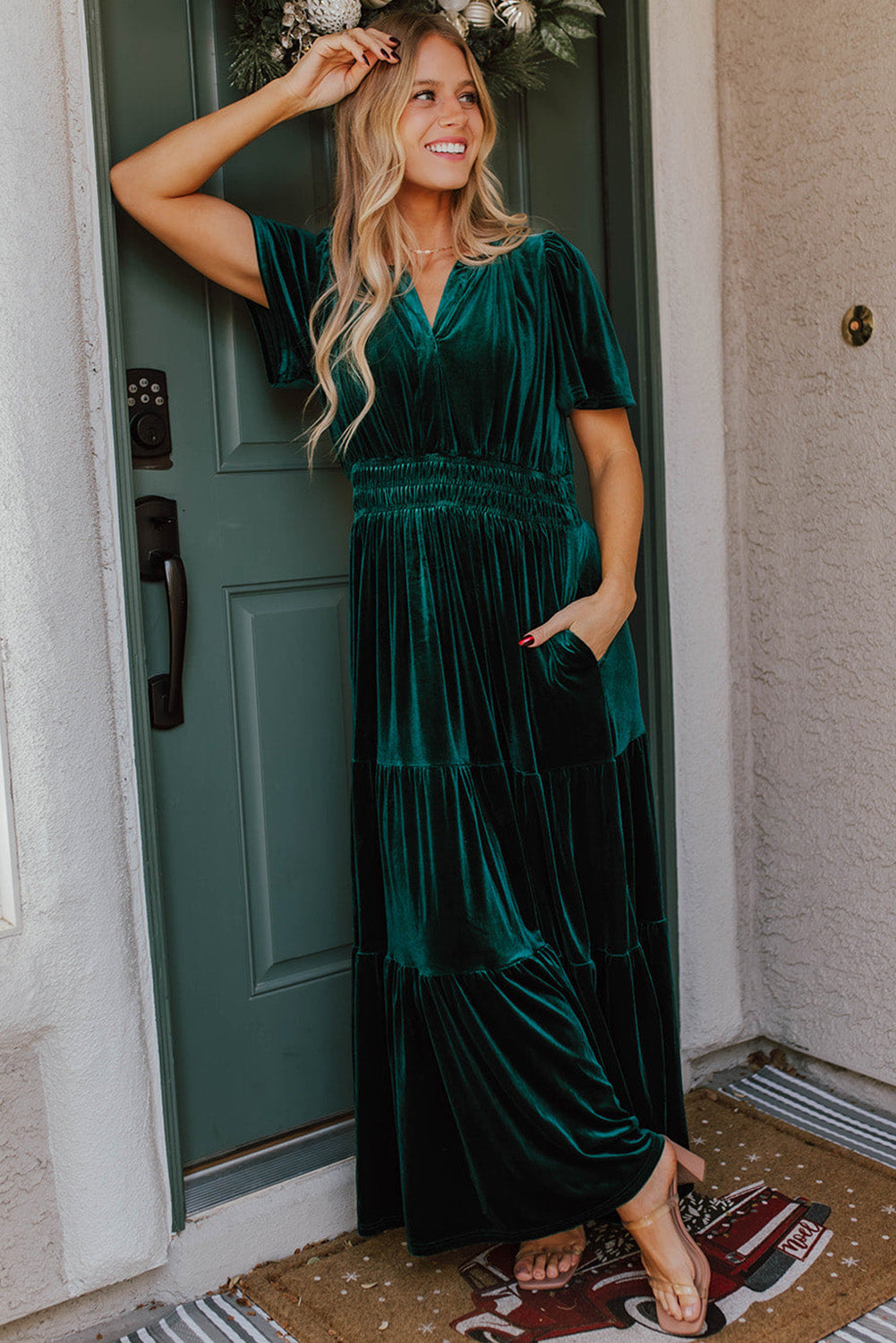 Woman wearing Elegant Emerald velvet maxi dress with V-neck and short sleeves, showcasing a boho-inspired tiered design.