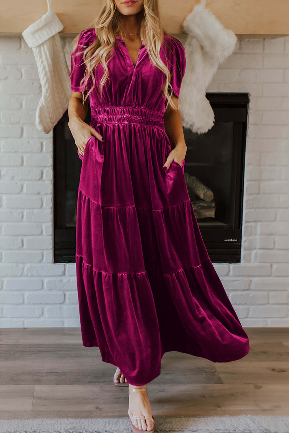 Elegant woman wearing DARLING DAHLIA Maxi velvet dress with tiered design and short sleeves, standing by a fireplace.