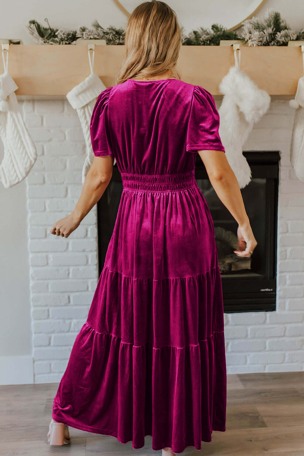 Woman wearing elegant velvet maxi dress with tiered design and short sleeves in a living room setting.