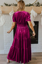 Woman wearing elegant velvet maxi dress with tiered design and short sleeves in a living room setting.