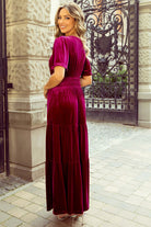 Woman wearing DARLING DAHLIA Maxi dress in elegant emerald, showcasing tiered velvet design and chic short sleeves against ornate iron gate.