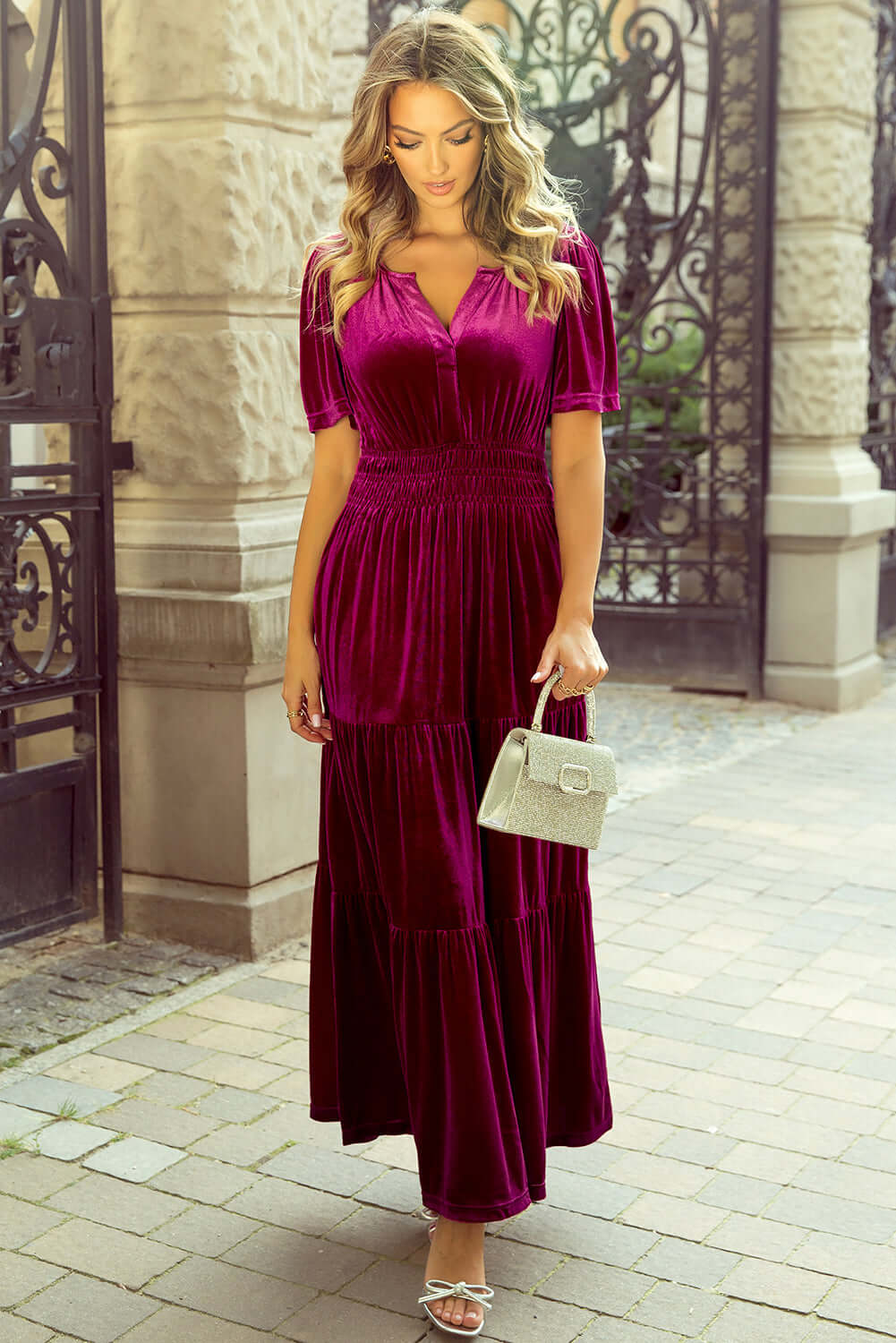 Elegant woman in a velvet maxi dress with chic short sleeves and tiered design, holding a handbag, showcasing boho-inspired fashion.