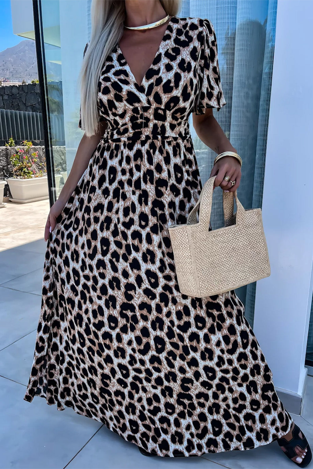 Stylish woman in a leopard print maxi dress holding a woven bag, showcasing wild elegance and confidence.