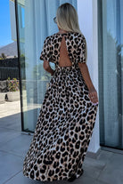 Back view of a woman in a leopard print maxi dress, showcasing its flowy design and open back details.