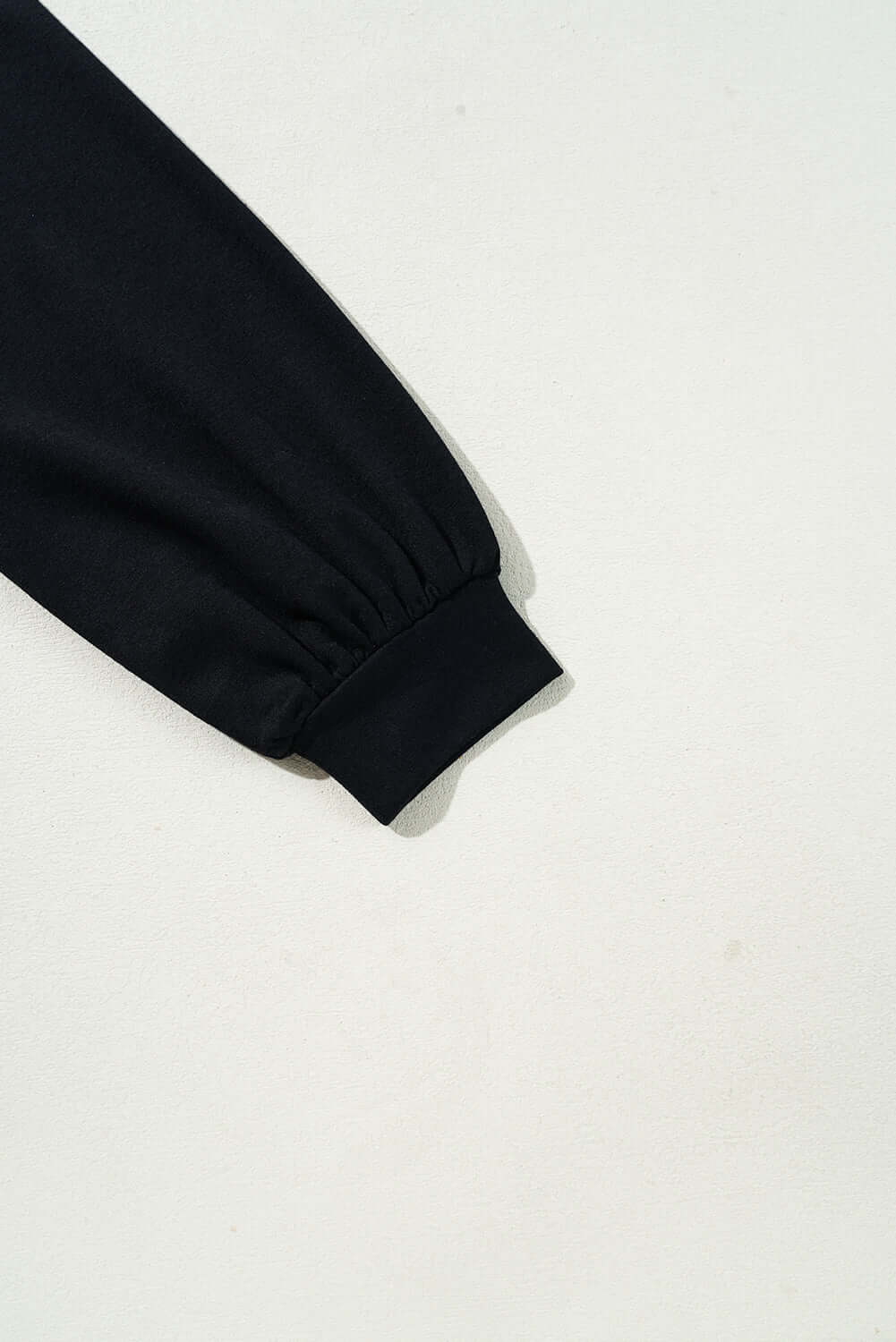 Close-up of the black sleeve cuff of a garment, showcasing its gathered design and soft fabric texture.