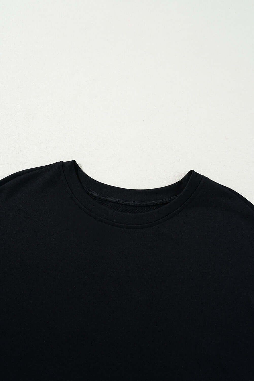 Black t-shirt close-up showcasing round neckline and soft fabric texture. Perfect for casual and versatile styling.