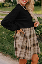 Woman wearing the PLAID CHARM Mini Dress by Vivian-Lu, featuring a black top and plaid patchwork skirt in a natural setting.