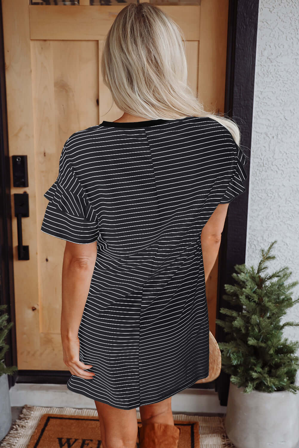 Back view of the Perfect Pathways black striped mini dress with ruffle sleeves and pockets, styled casually.
