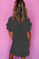 Back view of a woman wearing a black and white striped mini t-shirt dress with ruffle sleeves against a pink background.