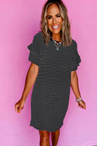 Woman smiling in a black striped mini t-shirt dress with ruffle sleeves against a pink background.