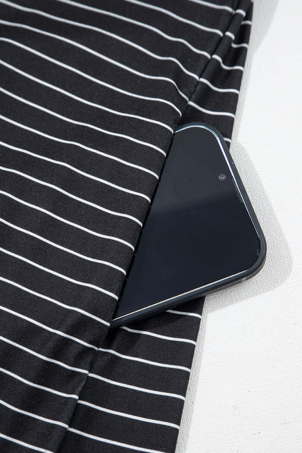Black striped mini dress with ruffle sleeves and a smartphone tucked into the pocket.
