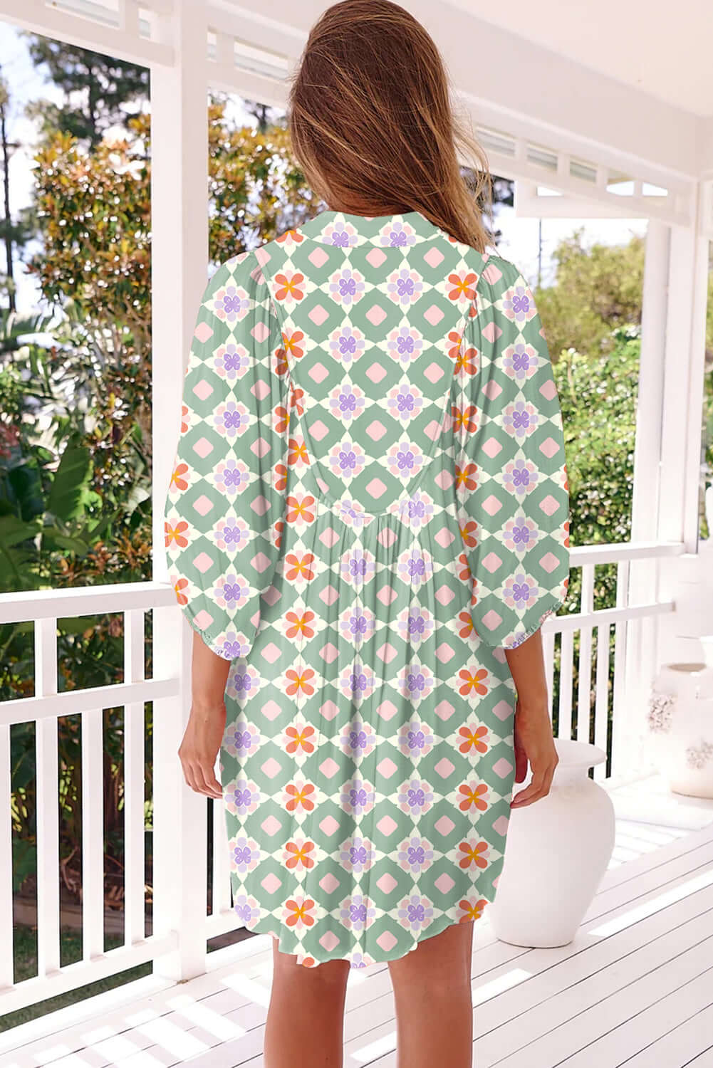 Back view of a woman in a mint mosaic dress with geometric floral patterns on a porch.