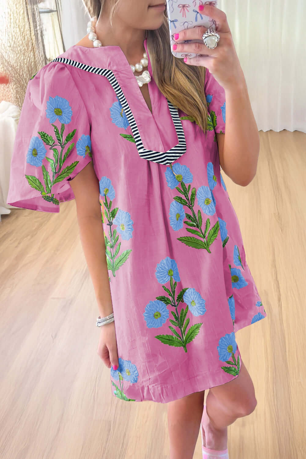 Woman wearing a floral Coastal Kiss Dress in magenta with blue blossoms, perfect for sunny outings and beach strolls.
