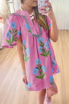 Woman wearing a floral Coastal Kiss Dress in magenta with blue blossoms, perfect for sunny outings and beach strolls.