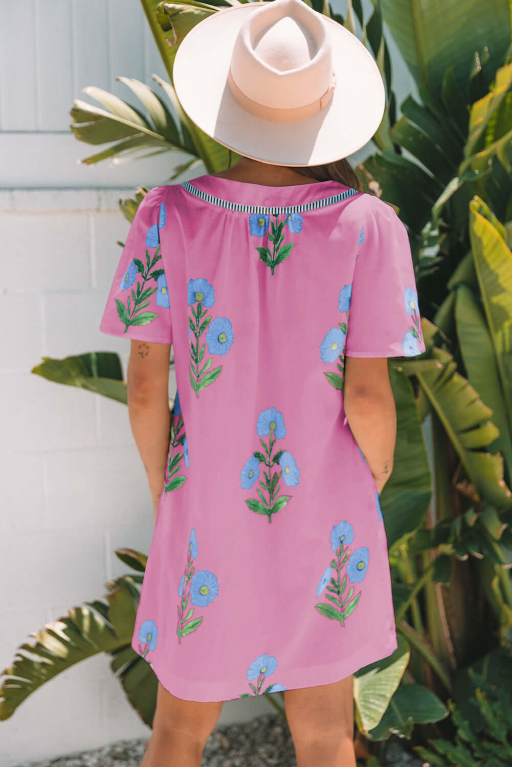 Back view of a woman in a magenta floral dress, wearing a wide-brim hat against tropical plants.