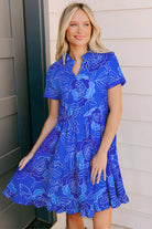 Model wearing a vibrant blue floral dress with a tiered skirt and V-neckline, perfect for a playful summer look.