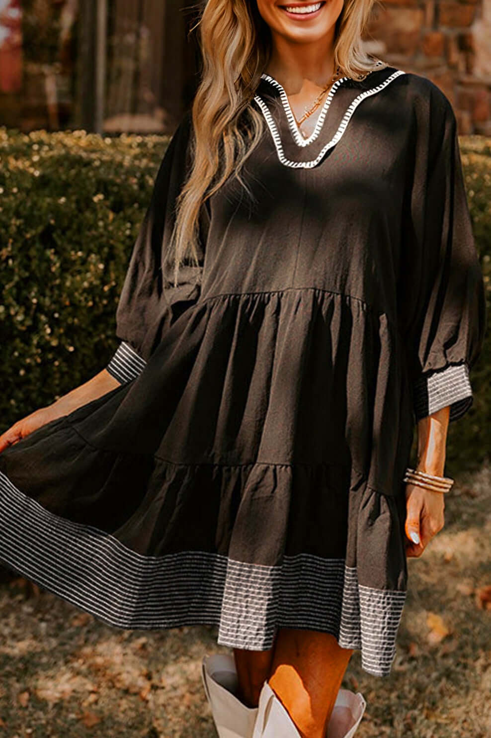 Chic black babydoll mini dress with contrast stitched V-neckline and striped hemline detail.