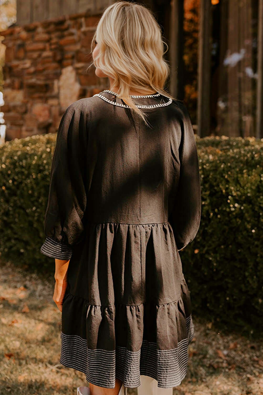 Back view of a chic black babydoll dress with tiered design and striped hemline detail.