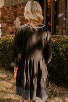 Back view of a chic black babydoll dress with tiered design and striped hemline detail.