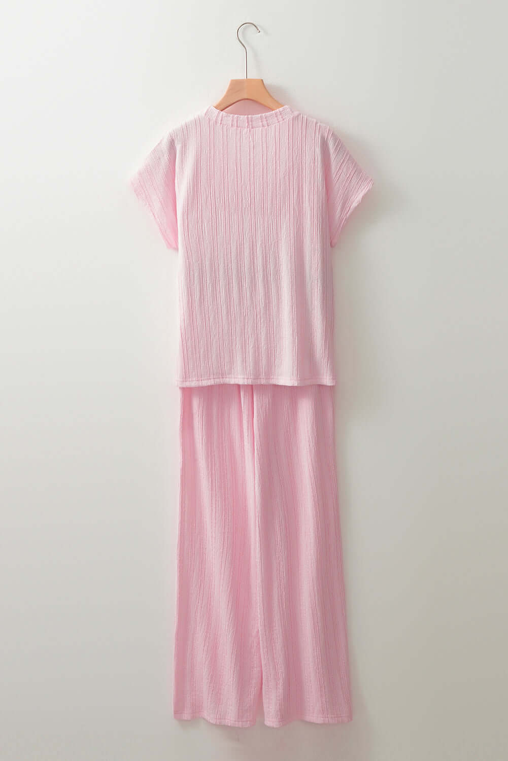 Soft Serenade Set: Light pink textured Henley top and wide-leg pants on a hanger, showcasing comfort and style.