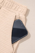 Textured beige shorts with a smartphone tucked into the pocket, showcasing casual style and convenience.