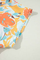 Close-up of vibrant floral fabric featuring orange and mint blooms on a tangerine background, part of a pants set.