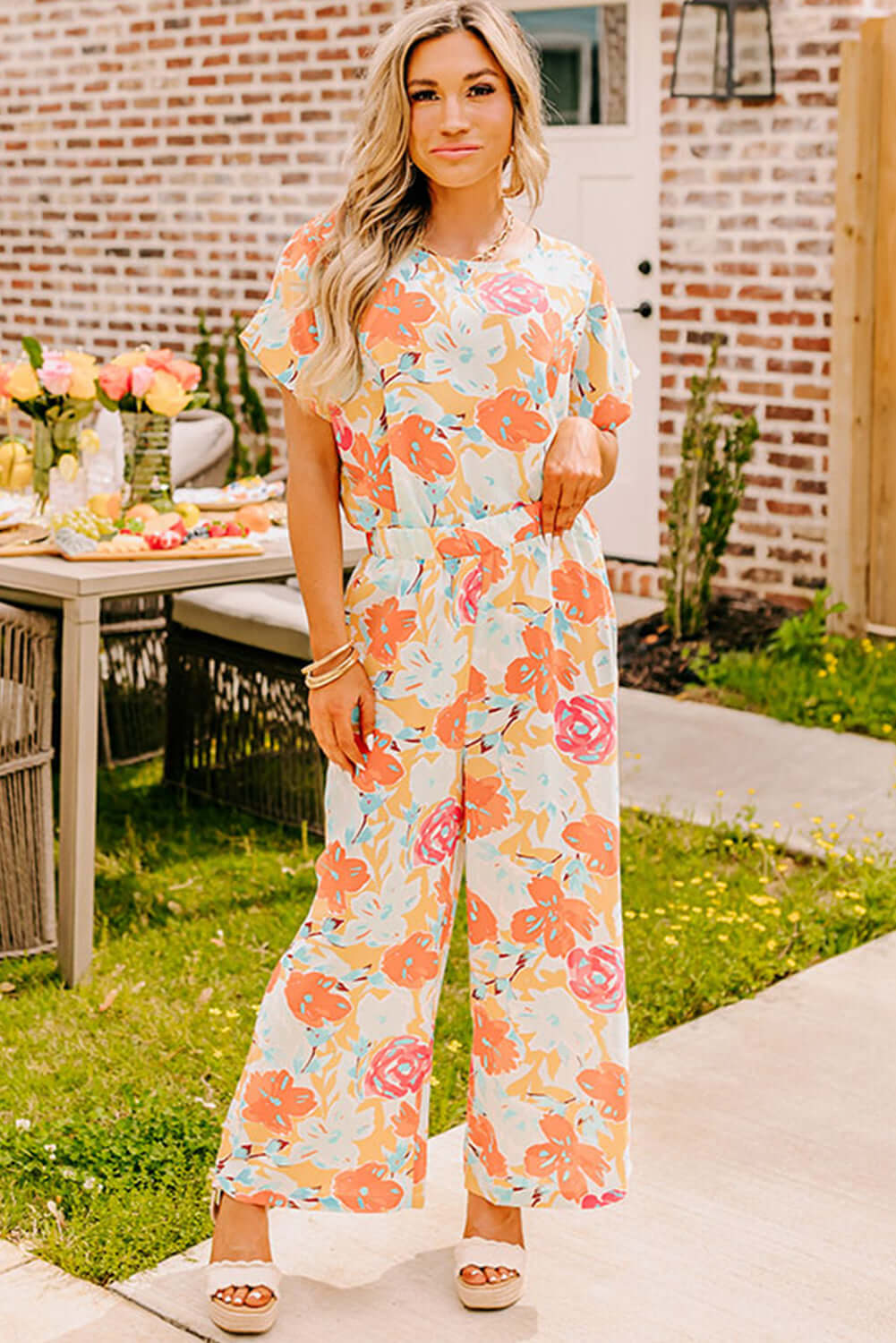 Woman in vibrant floral tangerine pants set, showcasing oversized blooms in coral and mint, perfect for casual outings.