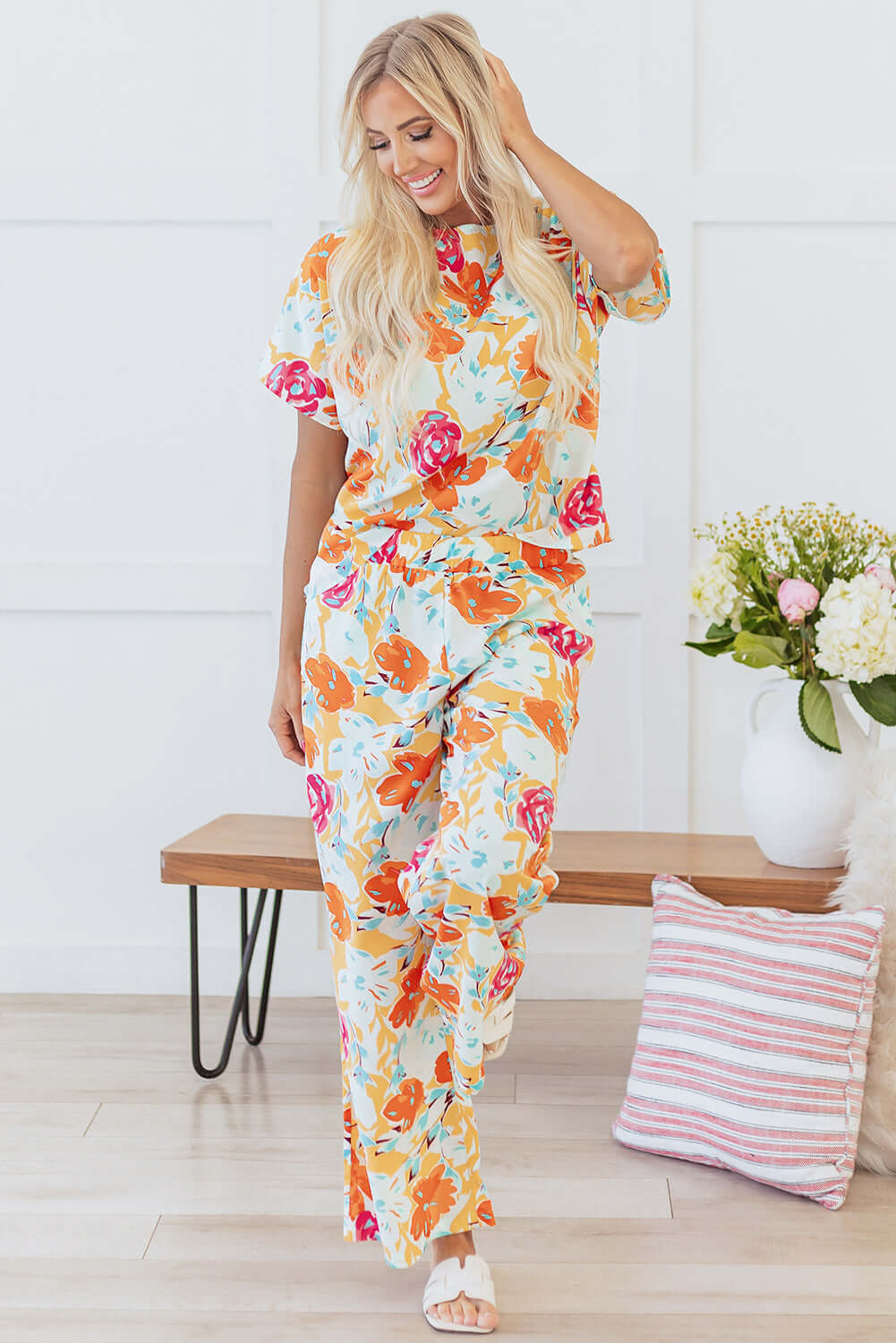 Woman in vibrant floral tangerine pants set, featuring oversized blooms, relaxed-fit top and wide-leg pants.