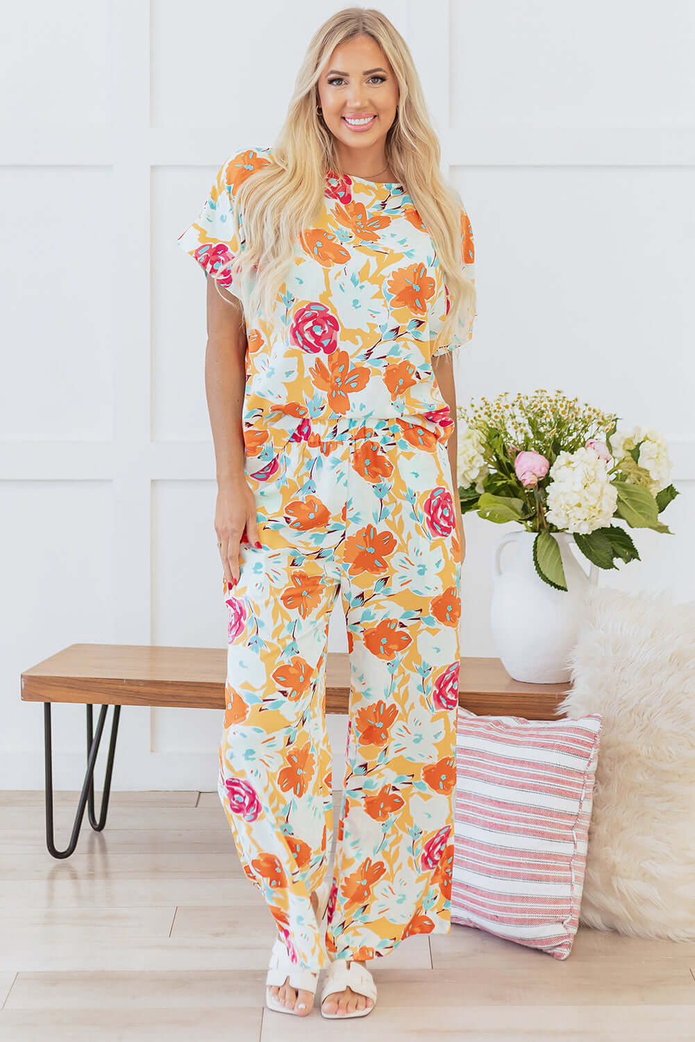 Model wearing Sunset Stroll Tangerine Floral Pants Set, featuring a relaxed top and wide-leg pants with vibrant flower patterns.