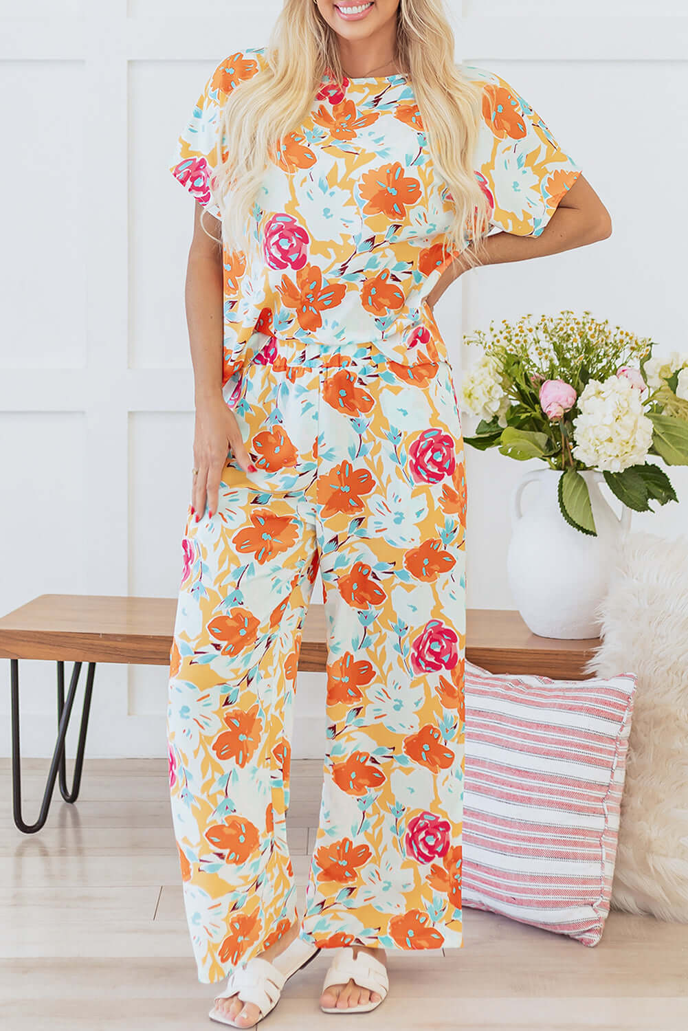 Model wearing Sunset Stroll Pants Set featuring vibrant tangerine floral print top and wide-leg pants in a bright, airy setting.