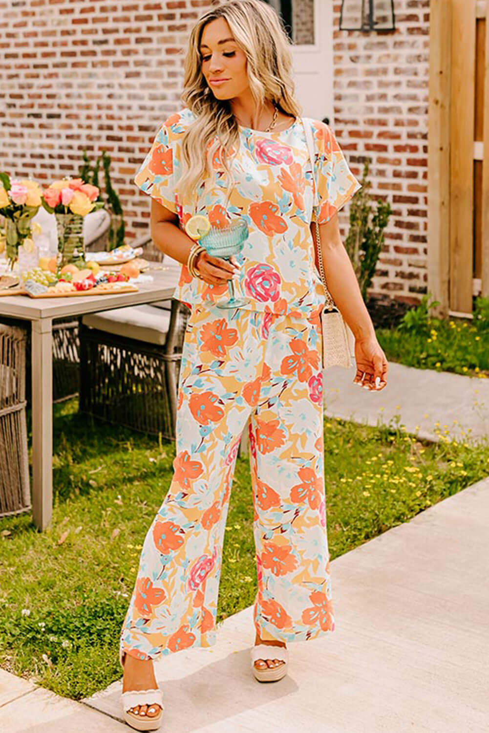 Woman in a vibrant floral printed sunset stroll pants set featuring coral and mint blooms, perfect for a stylish outing.