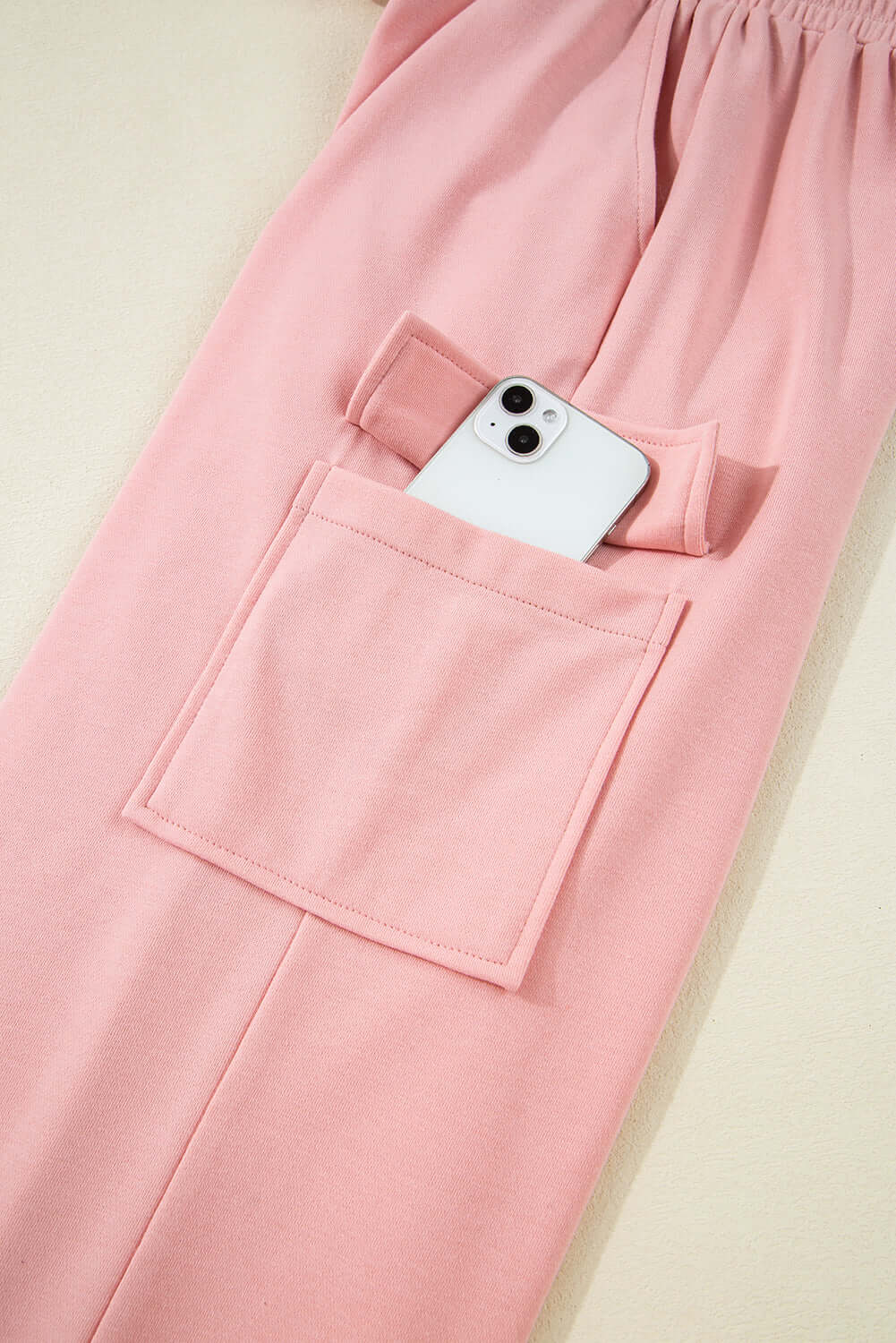 Close-up of pink cargo sweatpants featuring a side pocket holding a smartphone, showcasing comfort and style.