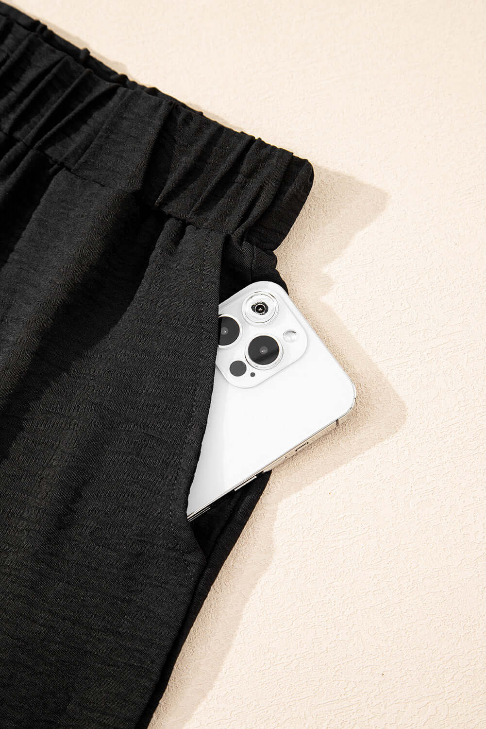Close-up of black wide-leg pants pocket featuring a smartphone, highlighting style and functionality.