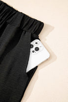 Close-up of black wide-leg pants pocket featuring a smartphone, highlighting style and functionality.