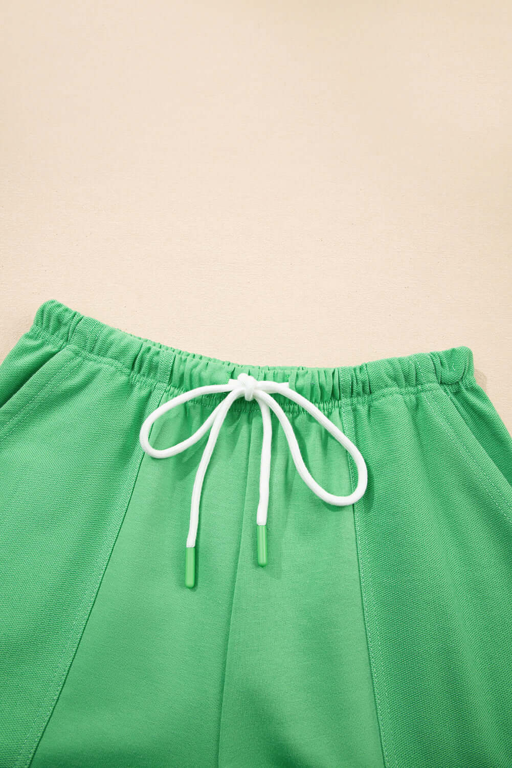 Close-up of green shorts with white adjustable drawstring, showcasing chic patchwork seaming for summer style.