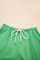 Close-up of green shorts with white adjustable drawstring, showcasing chic patchwork seaming for summer style.