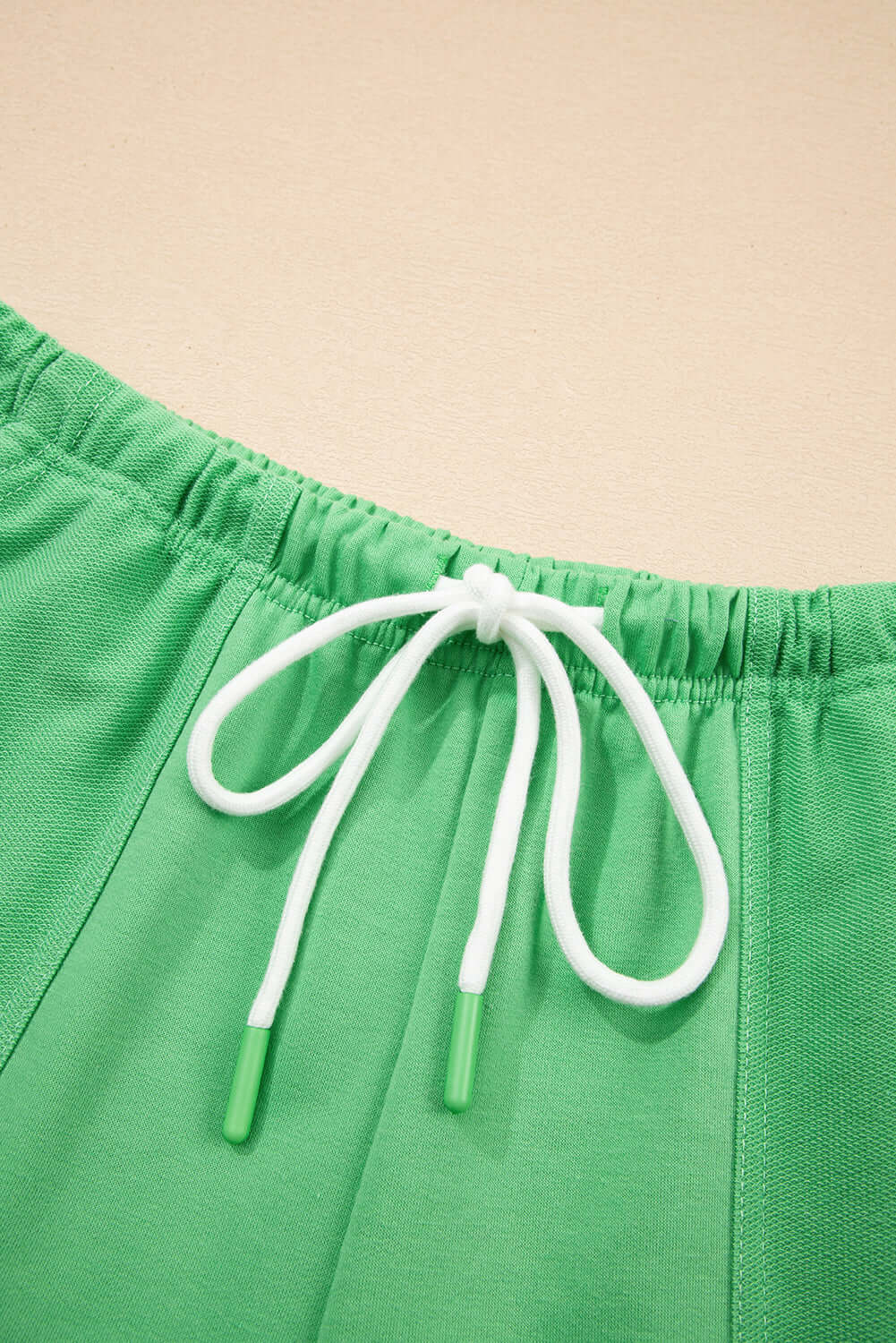 Close-up of green shorts with white drawstring, showcasing elastic waist and chic design details.