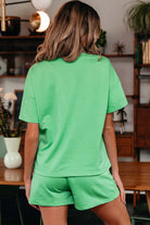 Back view of a woman wearing a bright green Zest for Life shorts set with a relaxed fit tee and shorts.