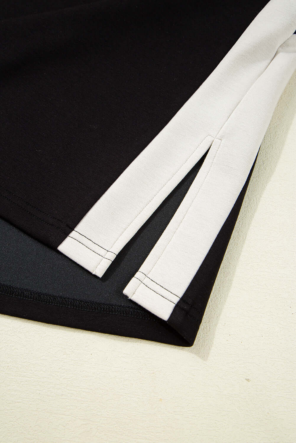 Close-up of Monochrome Motion Set showing zip collar and side slits in black and cream colorblock design.