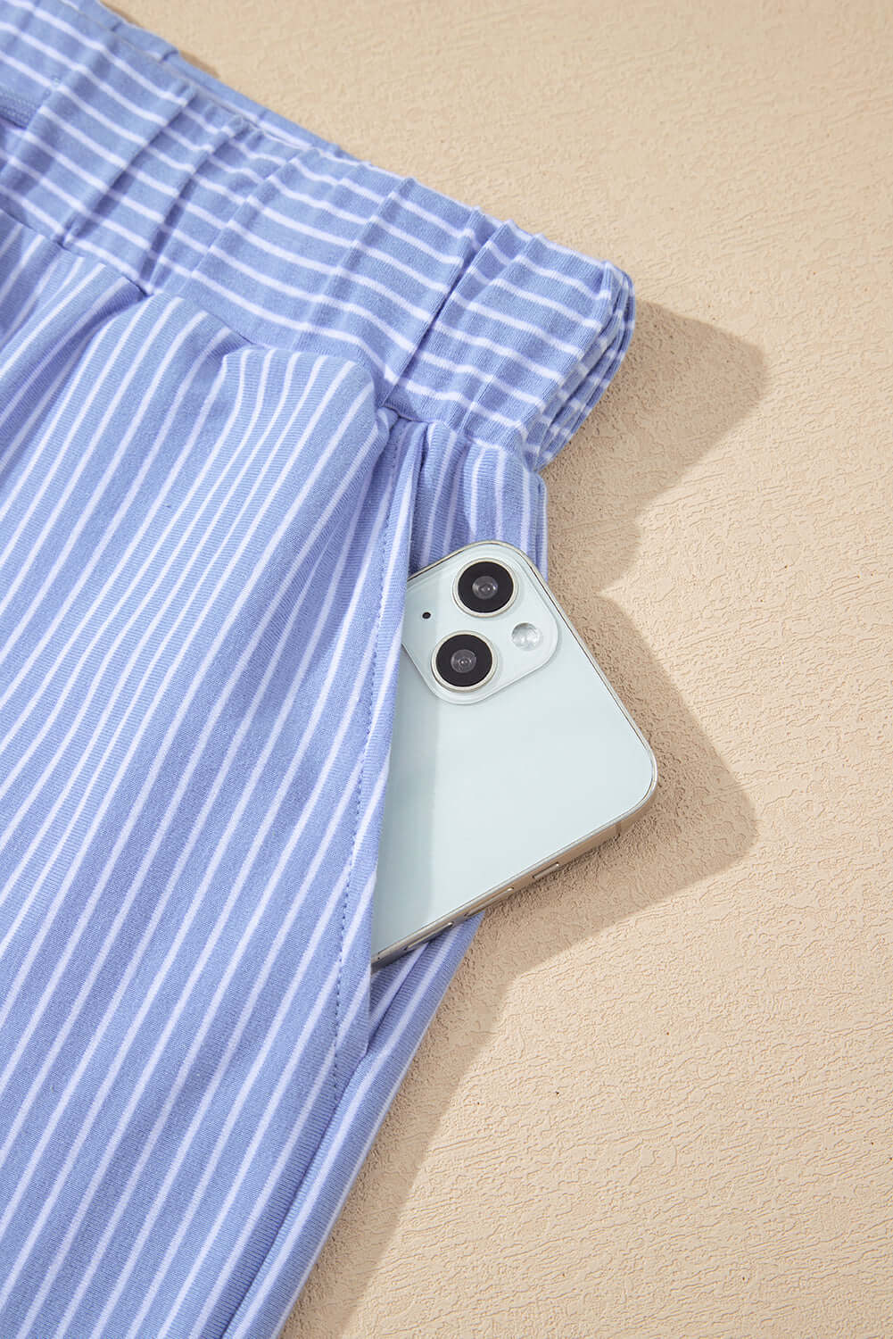 Sky blue striped shorts with a drawstring waist and iPhone peeking from the pocket, showcasing casual style.