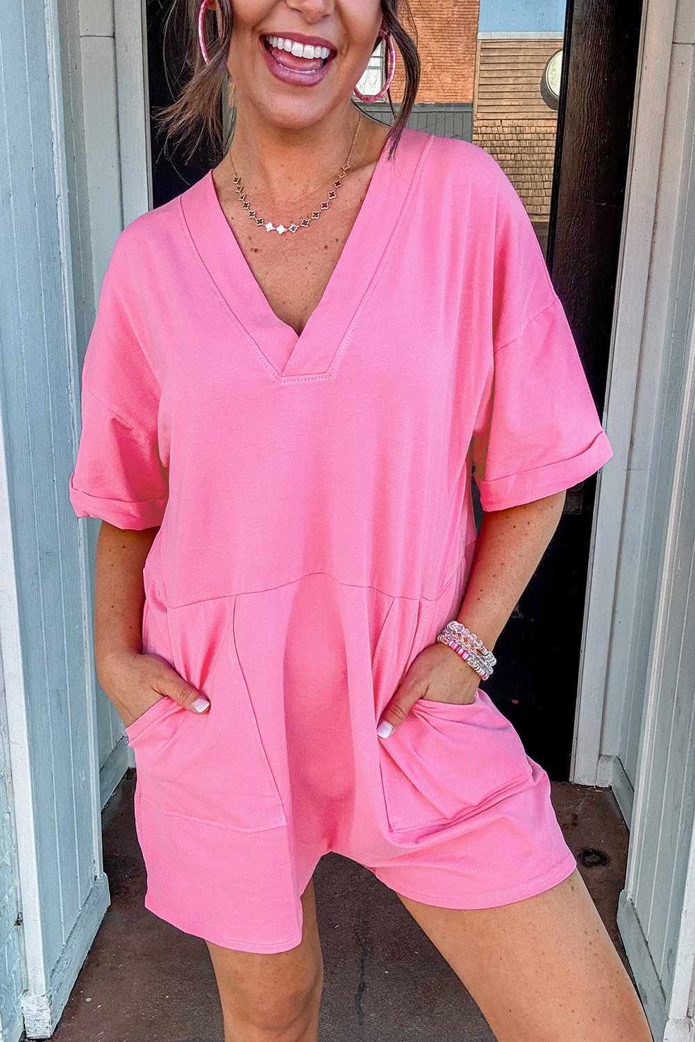 Woman smiling in a soft pink Dreamy Daze romper with short sleeves and deep V-neckline.