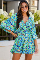 Woman wearing a green and blue abstract print Wave Dancer Romper with puff sleeves in a sunny outdoor setting.